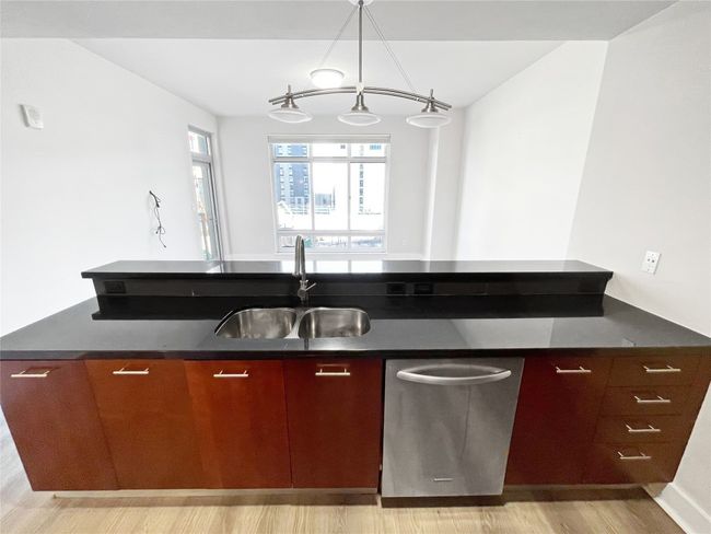 Kitchen featuring stainless steel dishwasher, a sink, dark countertops, and light wood-type flooring | Image 12