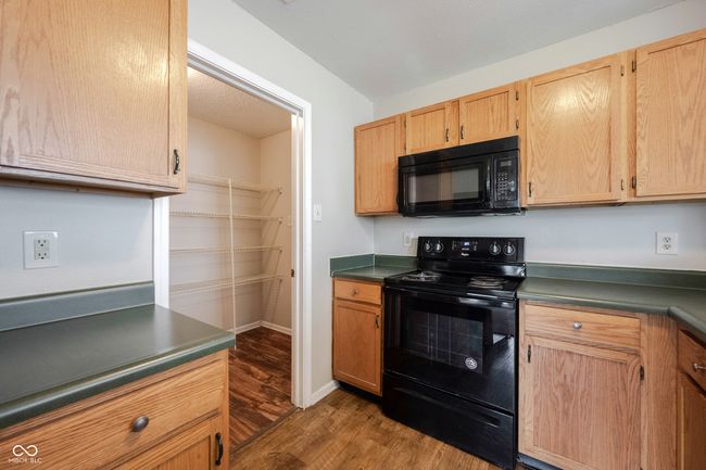 kitchen with dark wood-style flooring, dark countertops, baseboards, light brown cabinets, and black appliances | Image 16