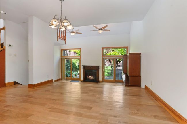 Unfurnished living room with a towering ceiling, a ceiling fan, light wood-style floors, baseboards, and a chandelier | Image 11