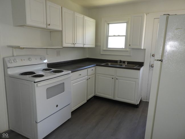 kitchen featuring white cabinetry, white appliances, dark wood-style flooring, a sink, and dark countertops | Image 6