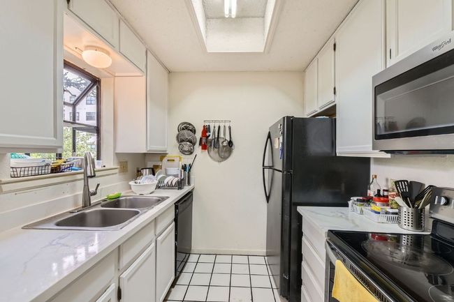 Kitchen featuring light tile patterned floors, a sink, white cabinetry, and stainless steel appliances | Image 12