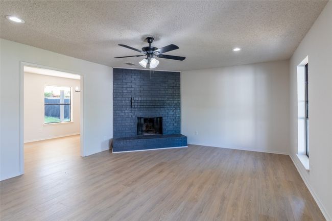 Unfurnished living room with ceiling fan, wood finished floors, a textured ceiling, and a fireplace | Image 25