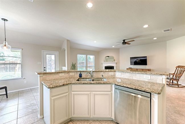 Kitchen featuring stainless steel dishwasher, ceiling fan, open floor plan, an island with sink, and light stone countertops | Image 25