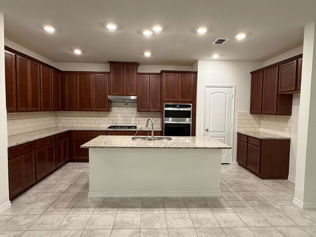 Kitchen featuring a sink, stainless steel double oven, under cabinet range hood, decorative backsplash, and light stone countertops | Image 8