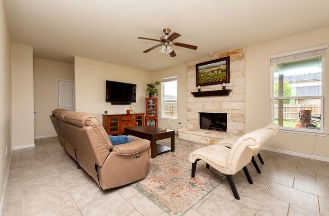 Living area with ceiling fan, light tile patterned floors, a stone fireplace, and baseboards | Image 13