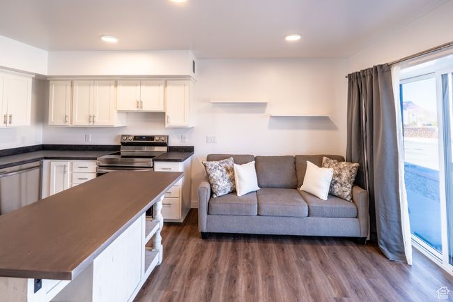 Kitchen featuring dark wood-type flooring, open shelves, dark countertops, stainless steel appliances, and white cabinets | Image 5