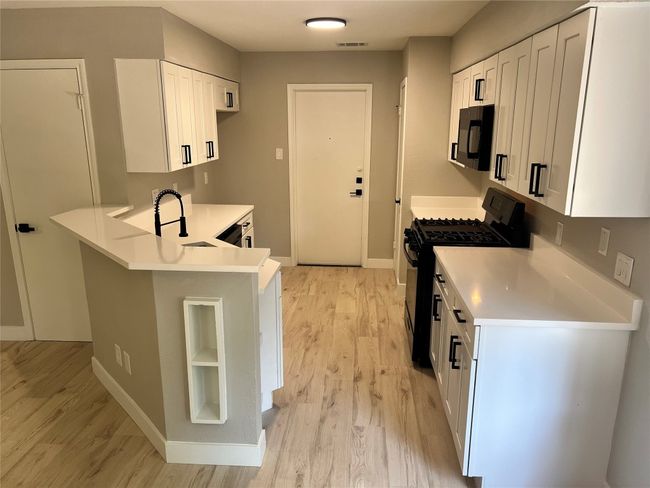 Kitchen with black appliances, light wood finished floors, and white cabinetry | Image 5