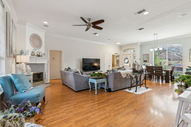 Living room with a ceiling fan, crown molding, light wood finished floors, and visible vents | Image 8