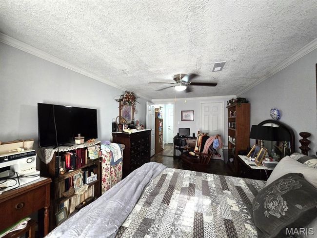 Bedroom with crown molding, a ceiling fan, wood finished floors, an office area, and a textured ceiling | Image 11