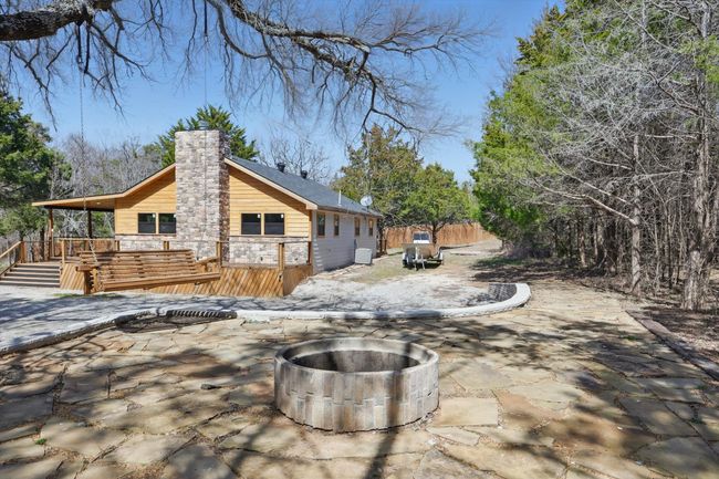 Rear view of house featuring an outdoor fire pit, stone siding, a chimney, fence, and a wooden deck | Image 10