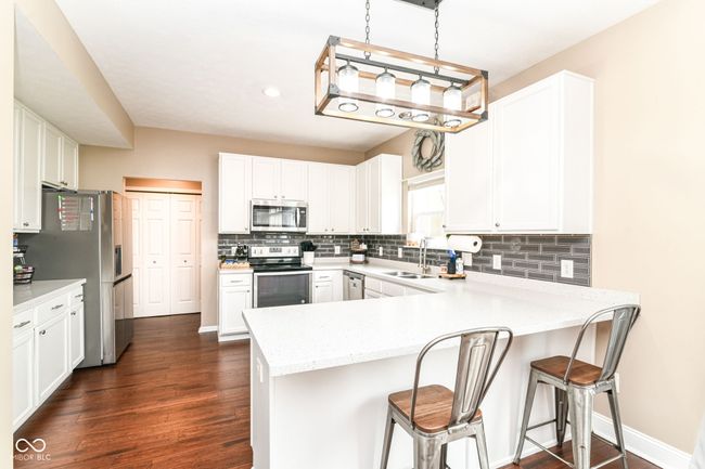 kitchen with appliances with stainless steel finishes, a peninsula, white cabinetry, backsplash, and recessed lighting | Image 11