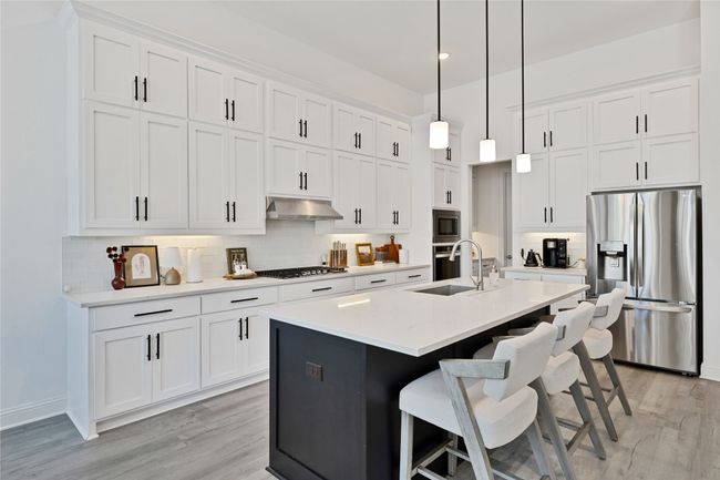 Kitchen with stainless steel appliances, a sink, light wood-type flooring, decorative backsplash, and white cabinets | Image 15