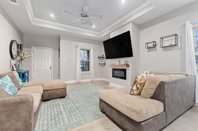 Living room featuring ceiling fan, ornamental molding, a raised ceiling, and a wealth of natural light | Image 6