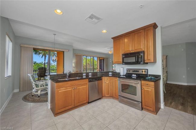 Kitchen with stainless steel appliances, a peninsula, brown cabinets, dark stone countertops, and recessed lighting | Image 15