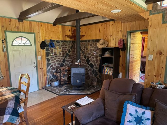 Living room featuring wood walls, a wood stove, wood finished floors, and beam ceiling | Image 14
