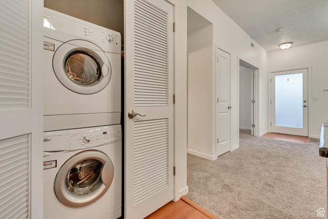 Clothes washing area featuring baseboards, stacked washer / dryer, laundry area, and light carpet | Image 21