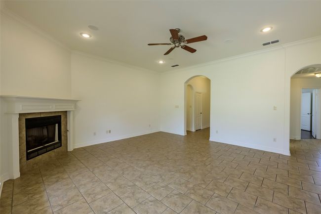 Unfurnished living room with arched walkways, a tiled fireplace, visible vents, ceiling fan, and crown molding | Image 16