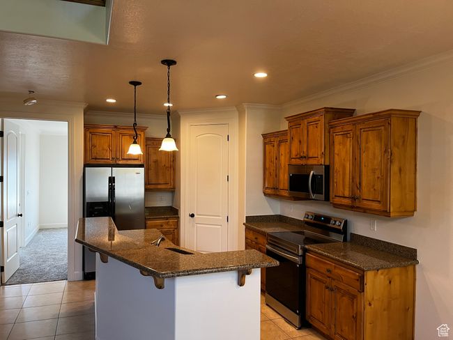 Kitchen with stainless steel appliances, brown cabinets, light tile patterned floors, a breakfast bar area, and ornamental molding | Image 21
