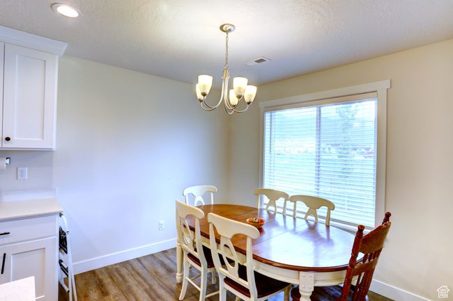 Dining space with a textured ceiling, light wood-type flooring, visible vents, a chandelier, and baseboards | Image 6
