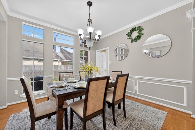 Bright dining room with large windows, elegant chandelier, and stylish decor. Features a classic wooden table set for four, with a neutral color palette and wainscoting details. | Image 19