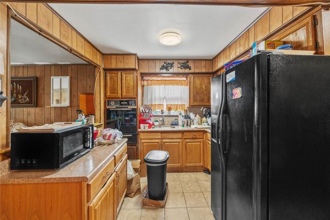 Kitchen featuring black appliances, wood walls, light tile patterned floors, brown cabinetry, and a warming drawer | Image 14