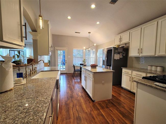This kitchen features modern granite countertops, a central island, and ample cabinetry. The wood flooring adds warmth, and large windows provide natural light. Stainless steel appliances complete the contemporary look. | Image 8