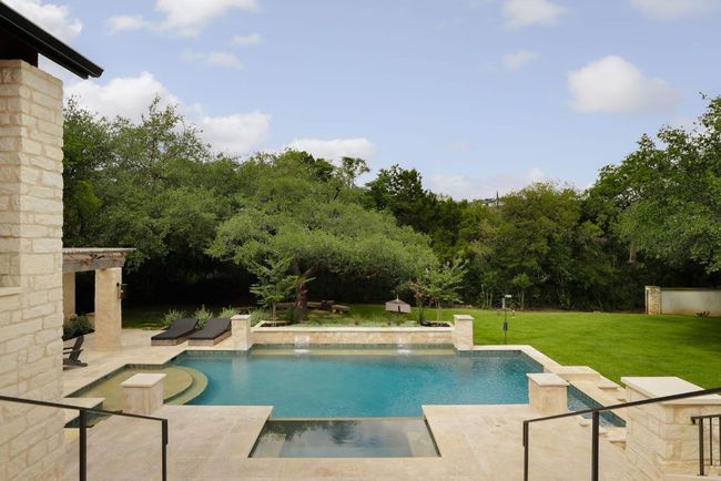 View of pool with a patio, a lawn, a pool with connected hot tub, and view of scattered trees | Image 30