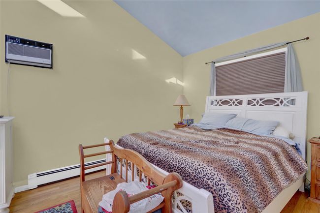 Bedroom featuring a wall unit AC, lofted ceiling, light hardwood / wood-style floors, and baseboard heating | Image 21