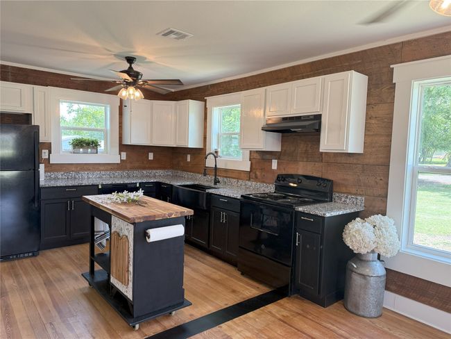 Kitchen featuring black appliances, under cabinet range hood, white cabinets, butcher block counters, and ceiling fan | Image 4