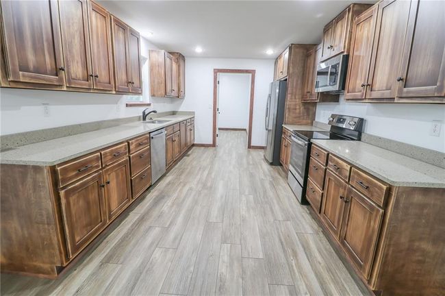Kitchen with light stone counters, stainless steel appliances, sink, and light hardwood / wood-style flooring | Image 14