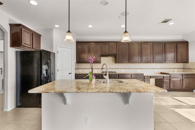 Kitchen with light tile patterned floors, visible vents, a kitchen breakfast bar, and black refrigerator with ice dispenser | Image 24