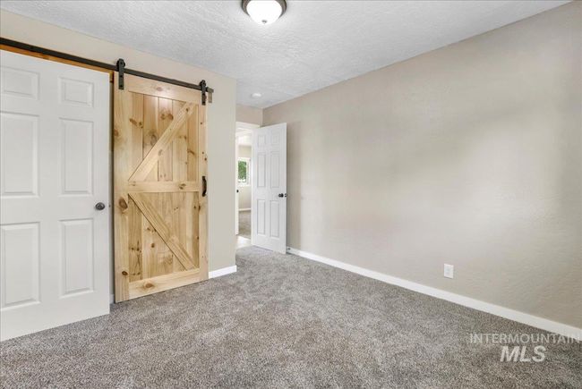 Unfurnished bedroom featuring carpet floors, a barn door, and a textured ceiling | Image 15