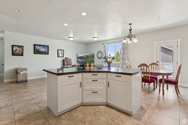 Kitchen featuring a chandelier, white cabinetry, a textured ceiling, dark countertops, and baseboards | Image 5