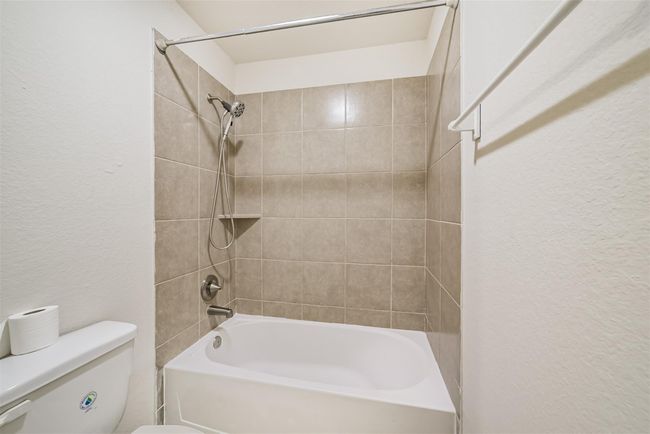 The upstairs secondary bathroom features a clean, tiled shower and bathtub with a handheld showerhead. The neutral tile design complements the white walls, creating a fresh and inviting space. | Image 23