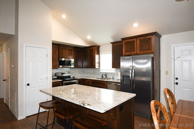 Kitchen with appliances with stainless steel finishes, a sink, backsplash, dark wood-style flooring, and vaulted ceiling | Image 13