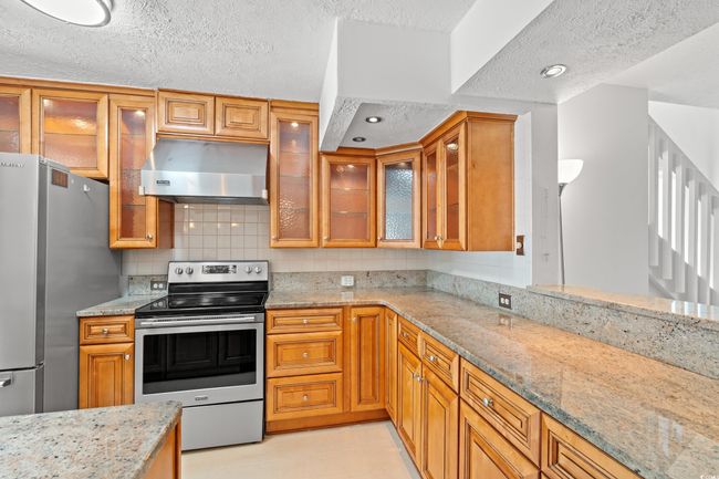Kitchen featuring appliances with stainless steel finishes, range hood, a textured ceiling, light stone countertops, and tasteful backsplash | Image 10
