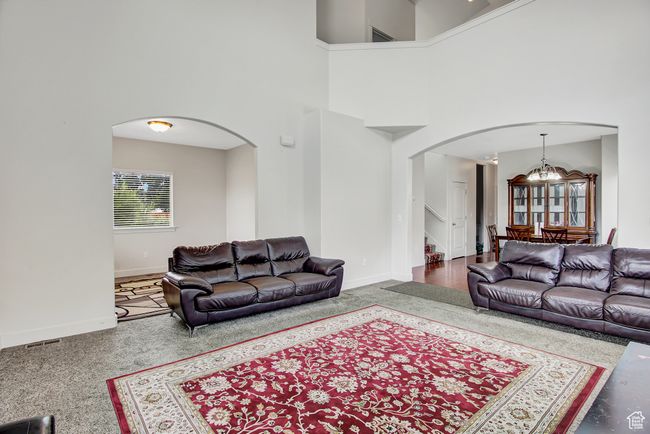 Carpeted living room featuring arched walkways, a chandelier, a towering ceiling, and stairs | Image 8