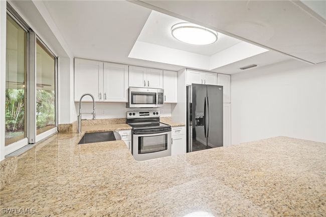 Kitchen featuring appliances with stainless steel finishes, a tray ceiling, white cabinets, and light stone counters | Image 4