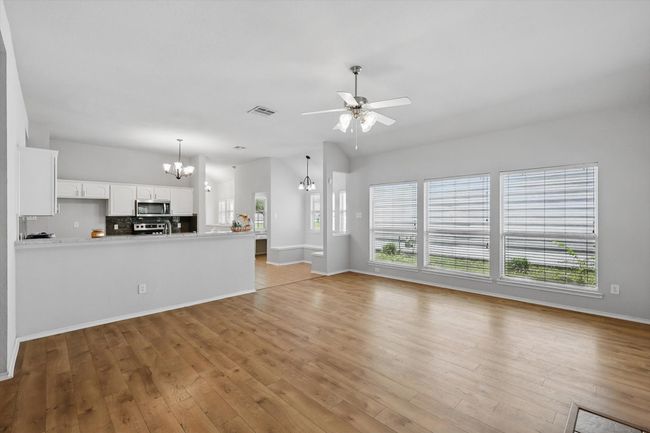 Unfurnished living room with a chandelier, healthy amount of natural light, light wood-style flooring, and a ceiling fan | Image 15