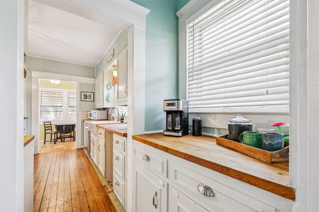 Kitchen featuring butcher block countertops, white cabinetry, light wood finished floors, white microwave, and ornamental molding | Image 11