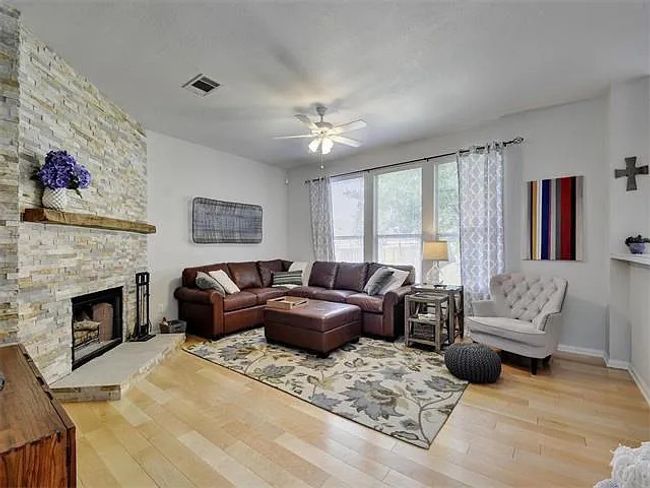 Living area featuring a ceiling fan, wood finished floors, and a stone fireplace | Image 7