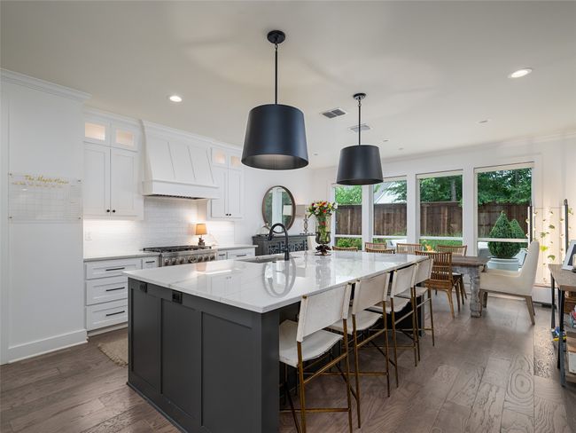 Kitchen featuring premium range hood, dark wood-style flooring, white cabinetry, a spacious island, and a breakfast bar | Image 9