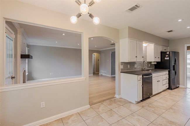 Kitchen with dishwasher, stainless steel fridge, arched walkways, white cabinetry, and dark countertops | Image 11