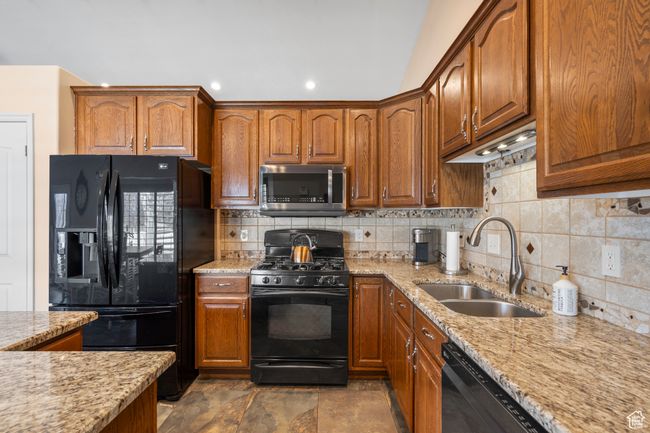 Kitchen with black appliances, a sink, decorative backsplash, light stone countertops, and recessed lighting | Image 11