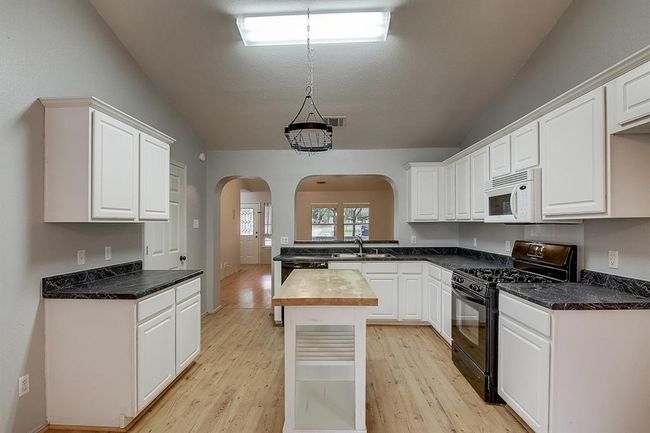 Kitchen with black gas stove, vaulted ceiling, arched walkways, a sink, and white microwave | Image 12