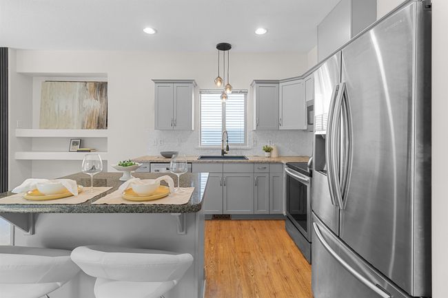 Kitchen with appliances with stainless steel finishes, a sink, gray cabinets, a kitchen bar, and light wood-style flooring | Image 16