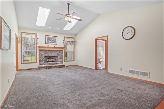 Unfurnished living room with a ceiling fan, vaulted ceiling with skylight, a stone fireplace, baseboards, and visible vents | Image 17