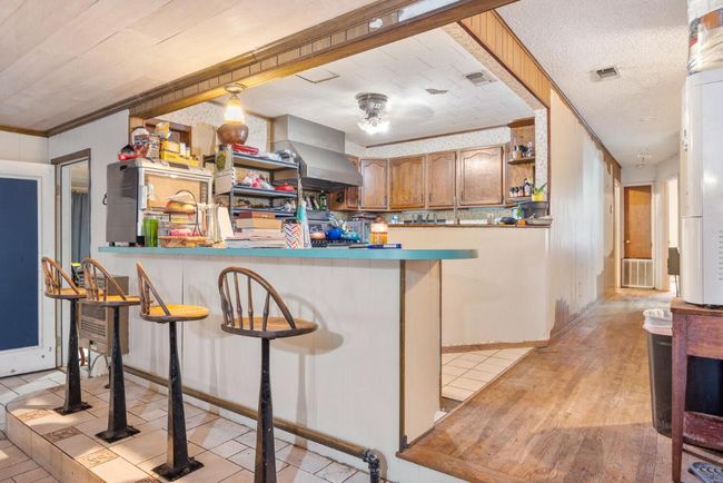 Kitchen with light wood-type flooring, visible vents, a peninsula, and wall chimney exhaust hood | Image 12