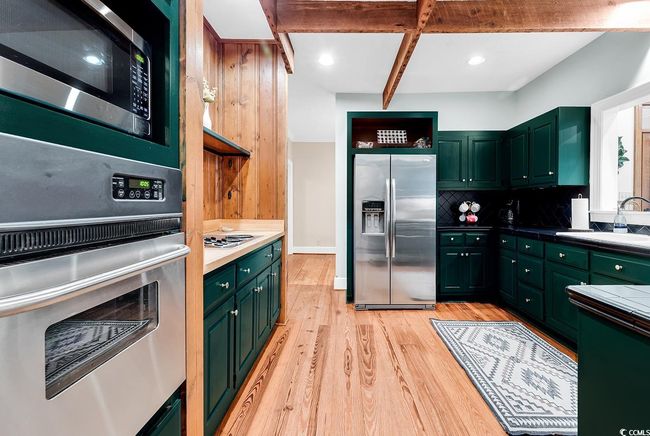 Kitchen featuring stainless steel appliances, green cabinets, light wood-type flooring, open shelves, and backsplash | Image 6