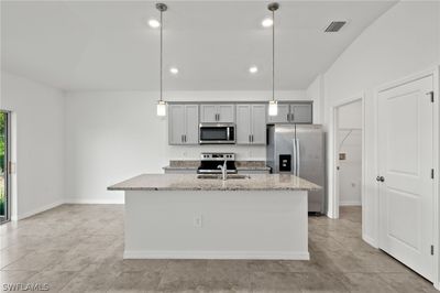 Kitchen featuring stainless steel appliances, light tile flooring, a center island with sink, and pendant lighting | Image 3